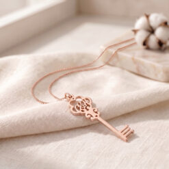 Collier Clé avec Initiales en plaqué or rose posé sur un tissu en lin beige
