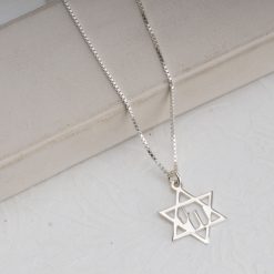 Collier Étoile de David avec symbole "Hai" intégré en argent massif 925, posé sur une surface épurée. Pendentif religieux judaïca avec gravure de précision et finition polie miroir sur une chaîne maille vénitienne. Bijou spirituel artisanal, cadeau symbolique pour Bar Mitzvah, Bat Mitzvah ou célébrations juives.