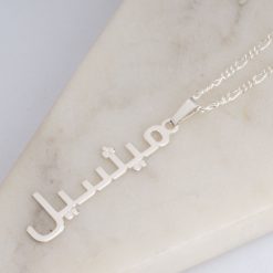 Collier prénom arabe vertical et chaîne figaro 2 mm en argent sterling posé sur un support en marbre.
