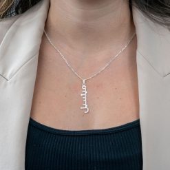 Collier prénom arabe personnalisé en argent 925 porté avec élégance avec un top noir décolleté et une veste beige.