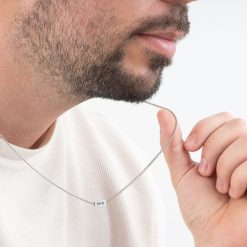 Zoom sur un homme ajustant son pendentif pilier gravé pour homme, montrant la texture de l'acier et les détails nets de la date "11.3.2022"