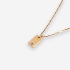 Collier pour maman avec initiale enfant et pierre de naissance en plaqué or. Sur l'image le collier est posé sur une surface claire. Idée cadeau fête des mères