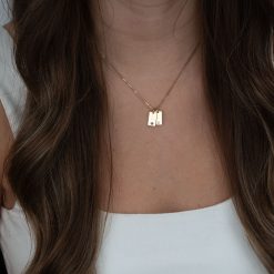 Collier pour maman avec initiale enfant et pierre de naissance en plaqué or. Sur l'image le collier est porté au cou d'un modèle aux cheveux longs chatains. Idée cadeau fête des mères le collier est personnalisable jusqu'à 5 pendentifs.