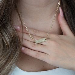 Gros plan sur les finitions polies d'un collier barre personnalisé en plaqué or 24ct, mettant en valeur la gravure de 2 initiales avec esperluette et les maillons allongés de la maille trombone.