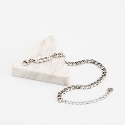 Bracelet Gourmette Homme Maille Cubaine sur fond blanc. Matière: acier inoxydable. Bracelet posé sur un triangle épai en marbre.