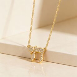 Collier pendentif Chai serti de zirconium en plaqué or et chaîne figaro 2 mm disposé sur une surface beige nette et épurée