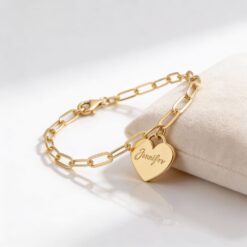 Bracelet cœur personnalisé avec pendentif gravé posé sur une surface en velours beige