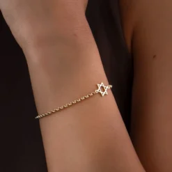 Bracelet étoile de David en plaqué or porté au poignet sur une peau halée. Design minimalist. Cadeau féminin qui saura faire plaisir. Image gros plan