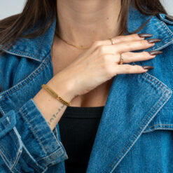 Bracelet Gourmette Identité Maille Cubaine en acier inoxydable finition doré porté par un modèle femme habillée d'une vest en Jean denim