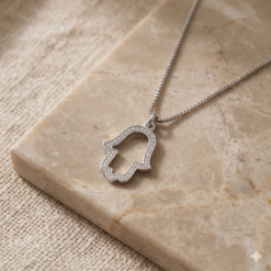 Collier Main de Fatma Ajourée et Oxydes de Zirconium en argent sterling 925 posé sur une surface en marbre beige